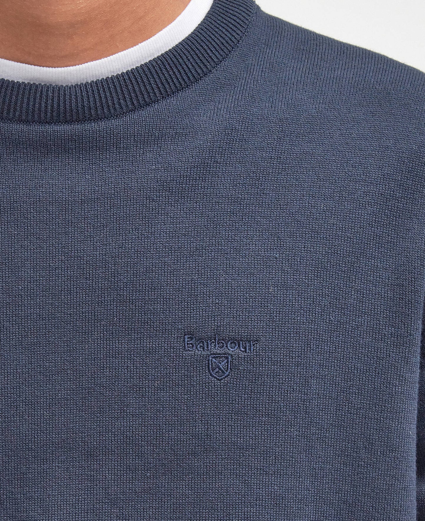 Close-up of a navy blue sweater with a Barbour brand logo on a white background