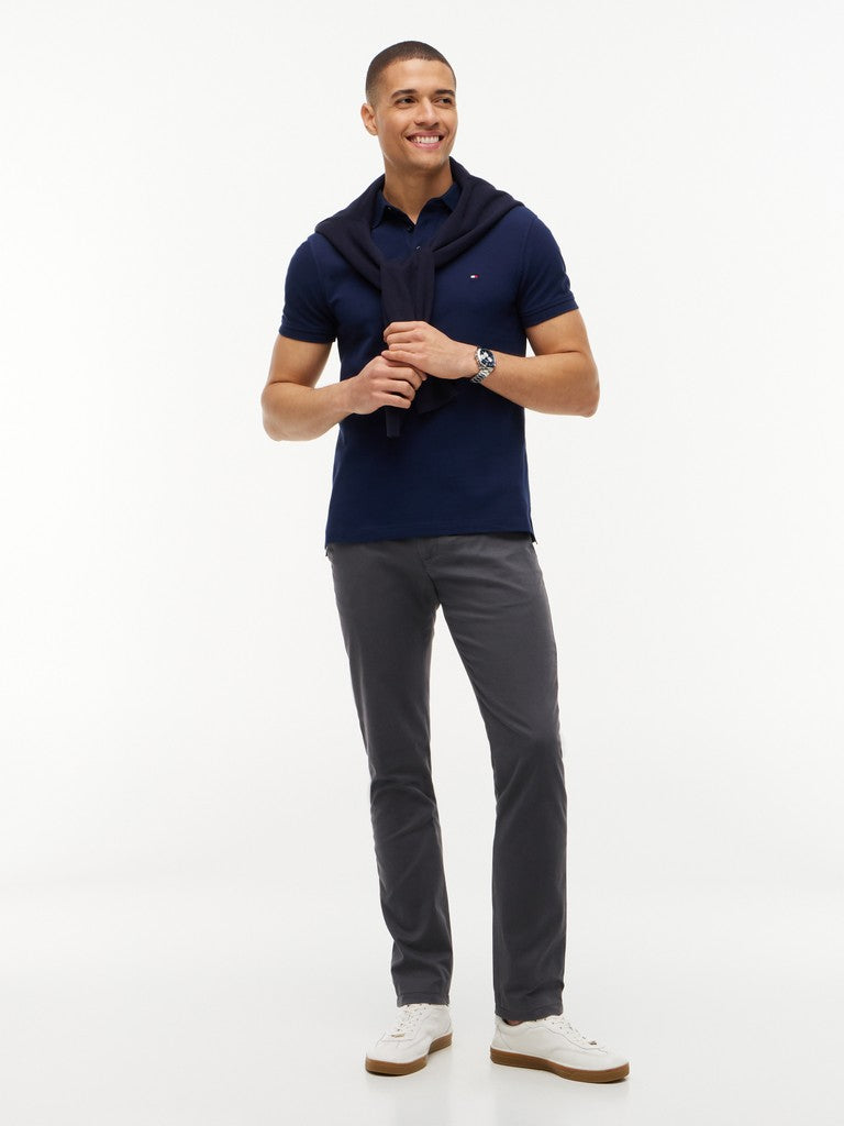 Man wearing a navy Tommy Hilfiger polo with navy jumper tied around his shoulders, gray slim leg chinos and white runners