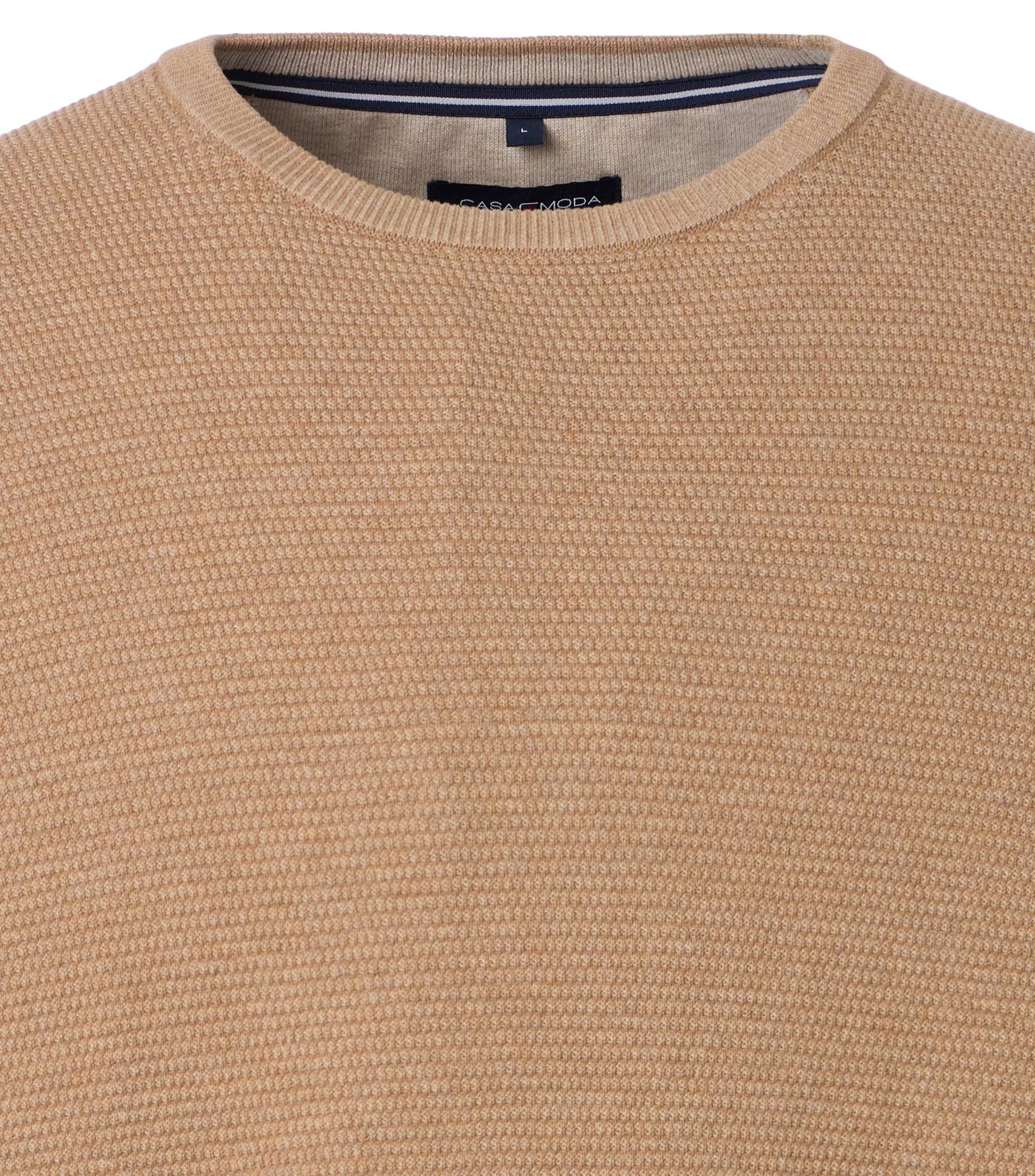 Close-up of a beige textured sweater with a brand label.