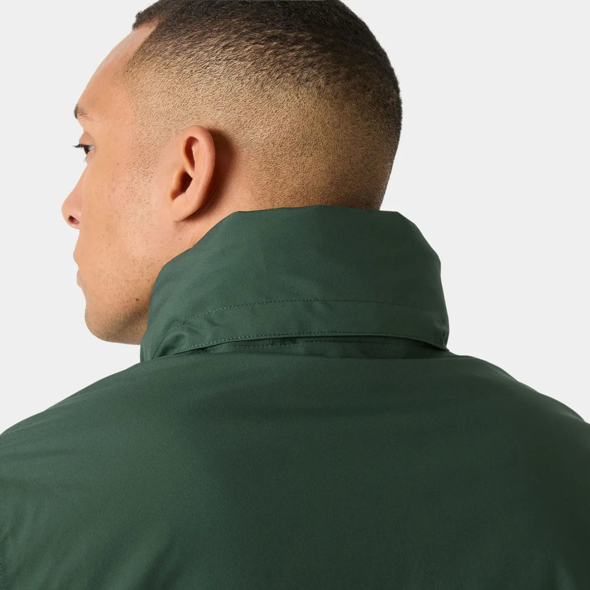 Close-up back and side view of a man wearing a dark green high-collar jacket against a light gray studio background.