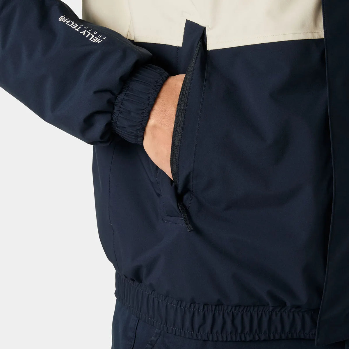 Close-up of a navy blue and off-white jacket with a hand in a zippered pocket, showing the elasticized cuffs and a white logo on the sleeve.