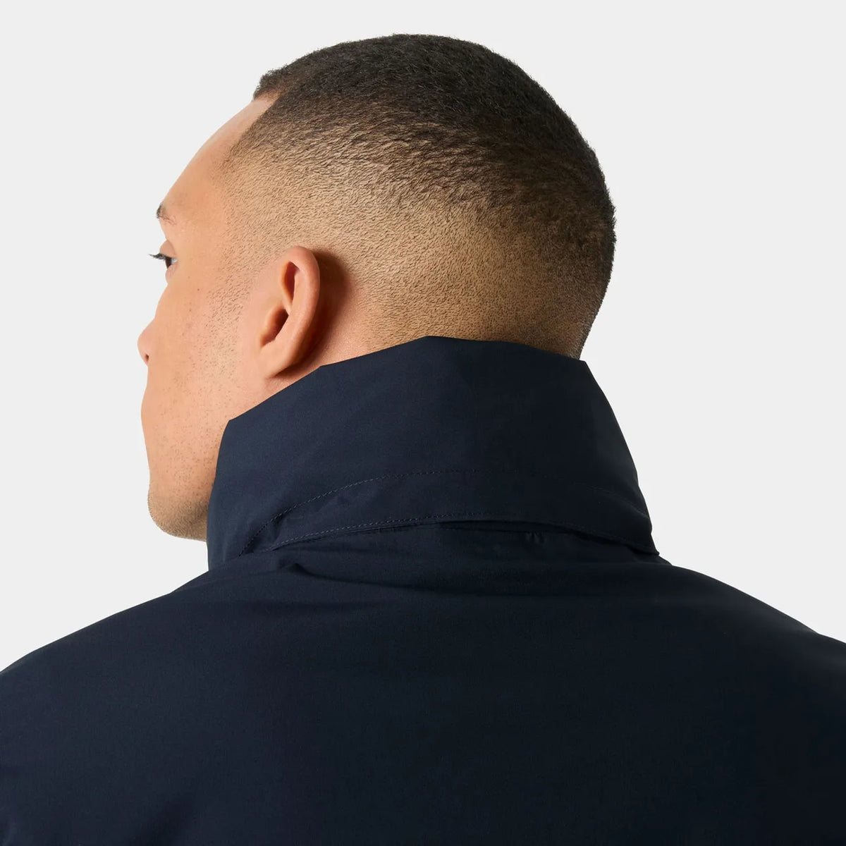 Close-up back view of a man wearing a dark navy high-neck jacket against a light gray background.
