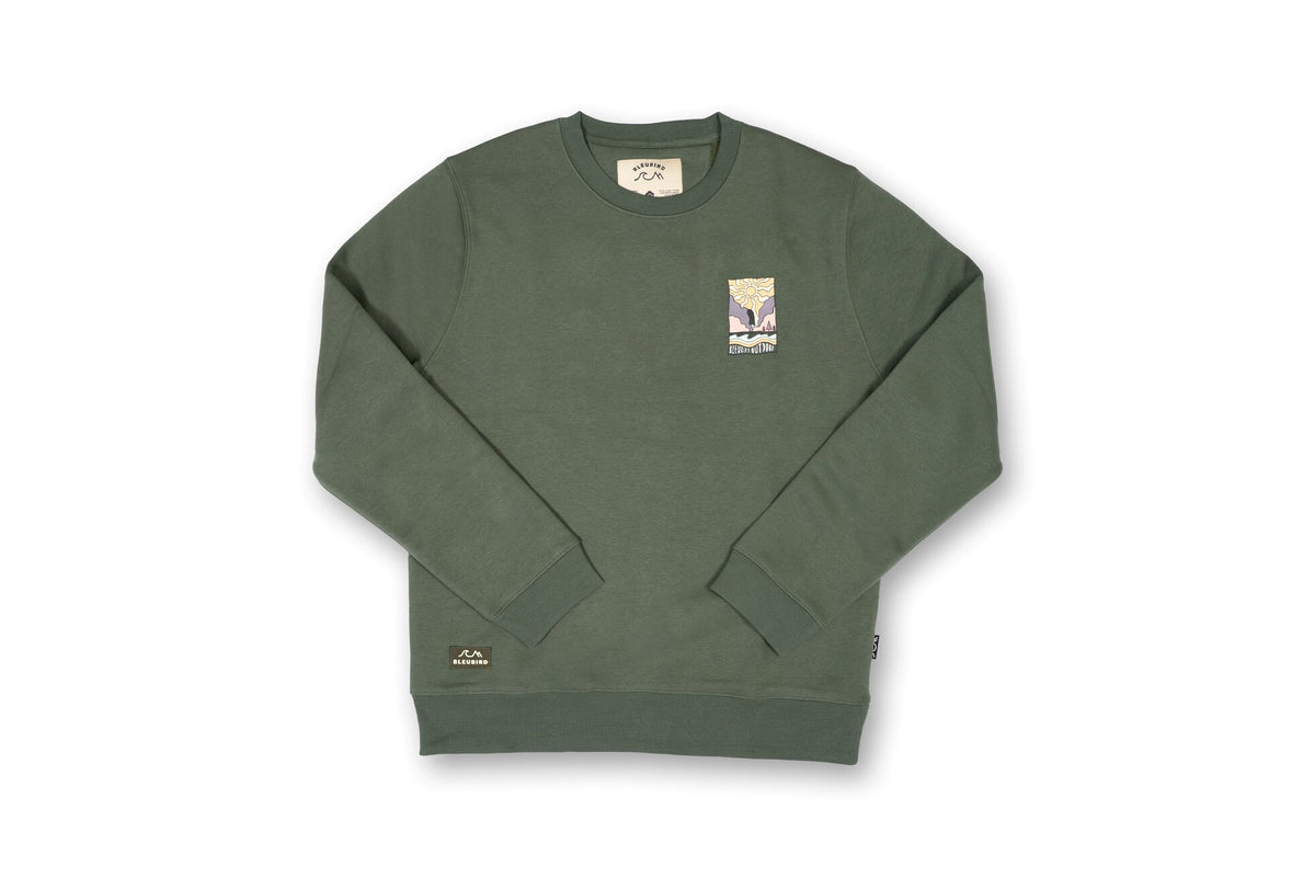 An olive green crewneck sweatshirt with a small graphic print on the left chest and a brand patch on the lower left hem, displayed flat against a white background.