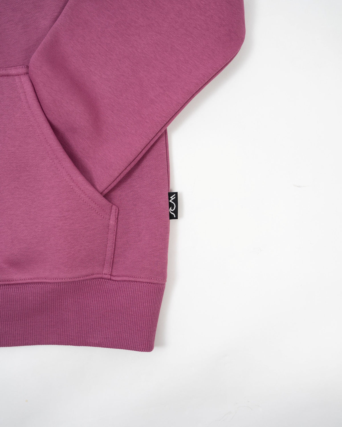 A close-up of a heathered magenta-purple hoodie showing the sleeve, ribbed cuff, and a small black brand tag with white text on a plain white background.