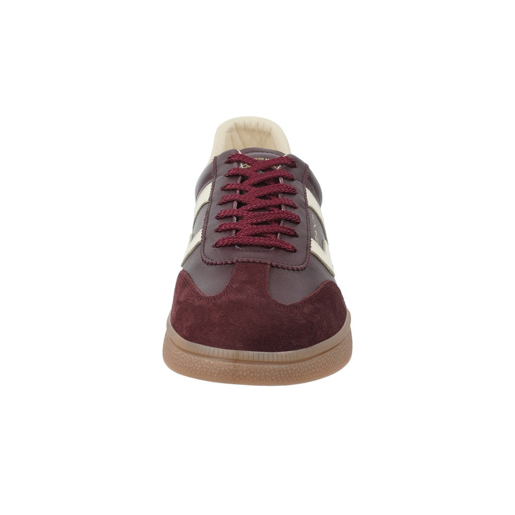 A single low-top sneaker shown from the front on a plain white background. The shoe features burgundy suede panels, dark brown leather overlays, burgundy laces, a cream-colored collar lining, and a light brown gum sole.