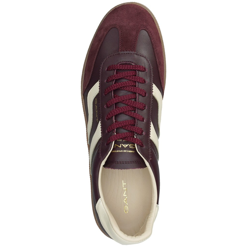 A single GANT sneaker shown from a top-down view, featuring burgundy leather and suede panels, burgundy laces, cream side stripes, and a cream interior with gold GANT branding.