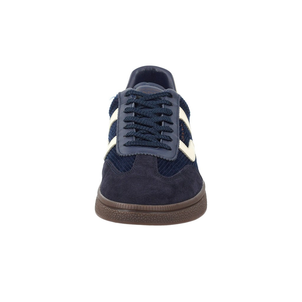A single low-top sneaker shown from the front on a plain white background. The shoe features a navy blue suede and cord upper with cream-colored side stripes, matching navy laces, and a brown gum sole.