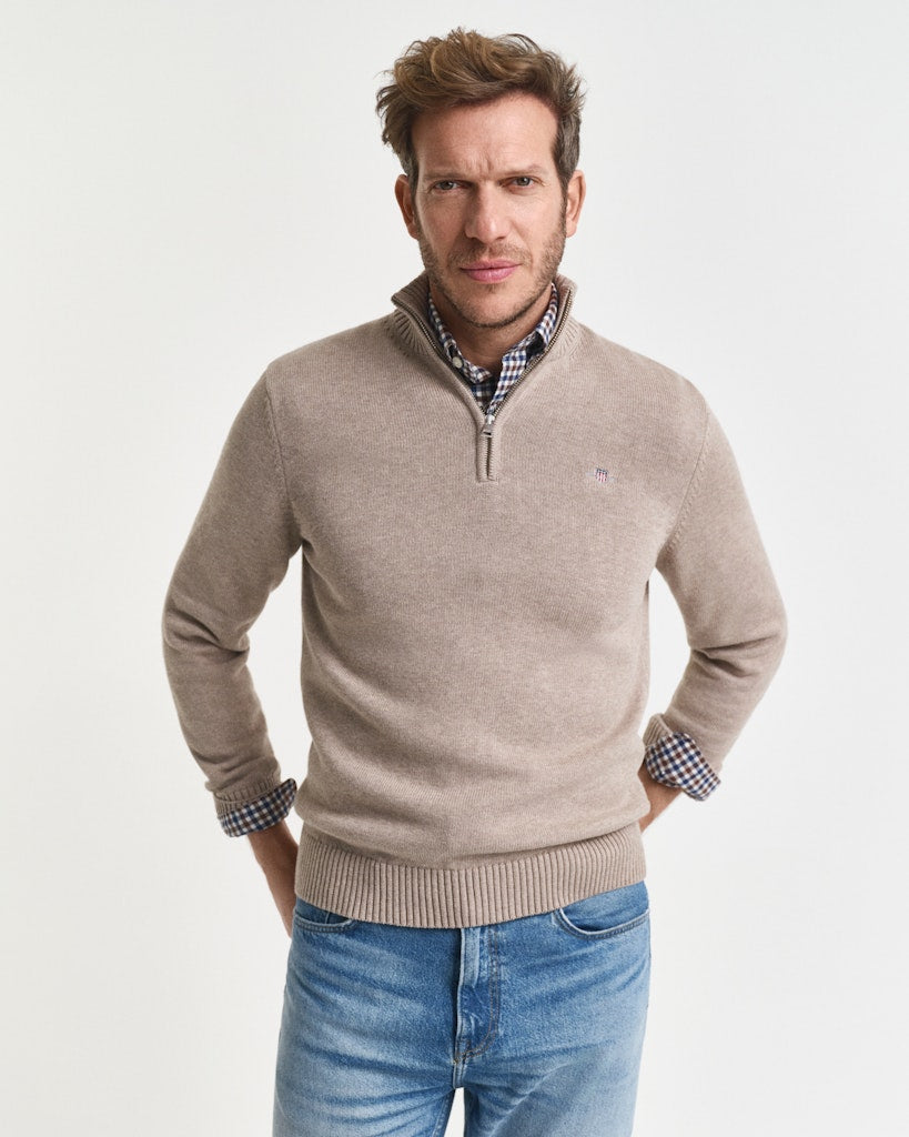 Man wearing a beige sweater with a checkered shirt underneath on a white background