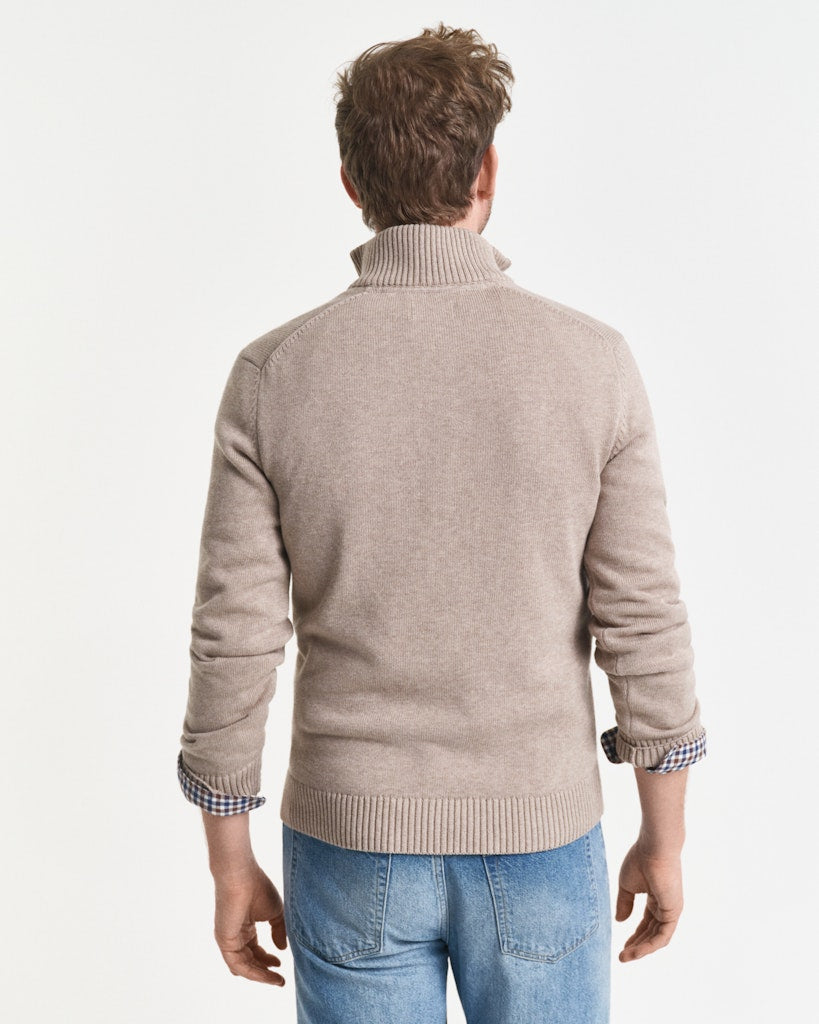 Man wearing a beige sweater and blue jeans on a light gray background