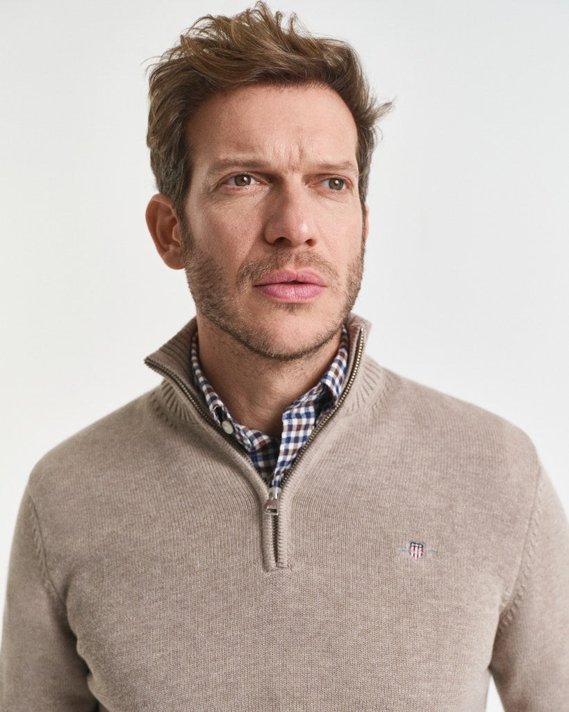 Man wearing a beige sweater with a GANT  brand logo on a light gray background