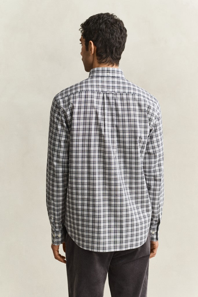 A man viewed from the back wearing a long-sleeve plaid button-up shirt in black, white, and gray, paired with dark gray trousers, against a plain beige studio background.