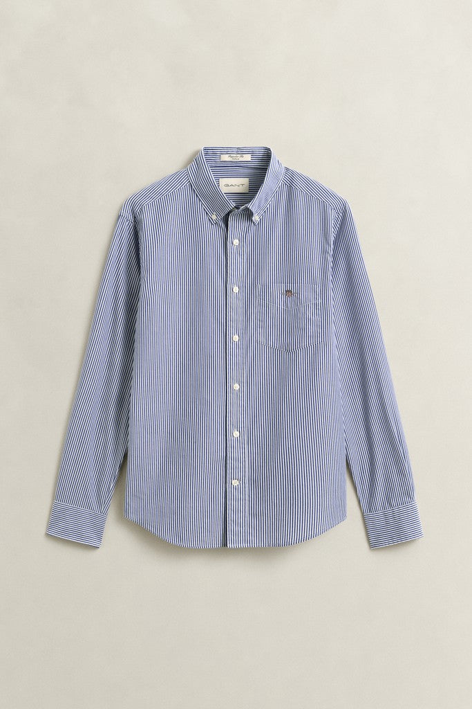 A light blue and white vertically striped long-sleeve button-down shirt with a chest pocket featuring the GANT logo, laid flat against a neutral beige background.
