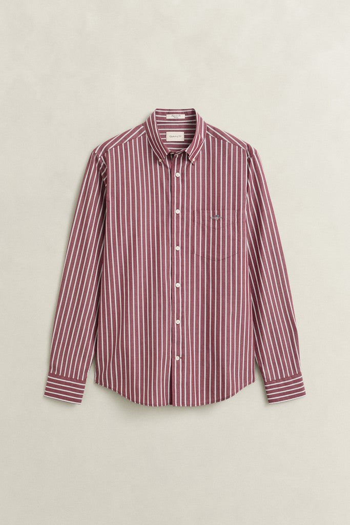 A long-sleeve button-up shirt with vertical stripes in deep wine and white, featuring a classic collar, white buttons, and a small embroidered GANT logo on the left chest, displayed against a light beige background.