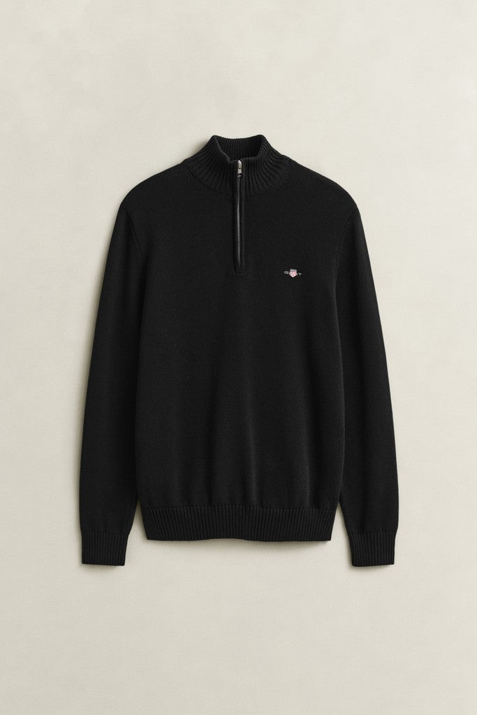 A black long-sleeve quarter-zip knit sweater with a small embroidered Gant logo on the left chest, displayed flat against a light beige background.