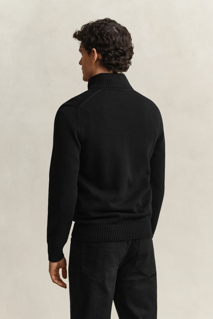 Man wearing a black zip neck sweater against a beige background