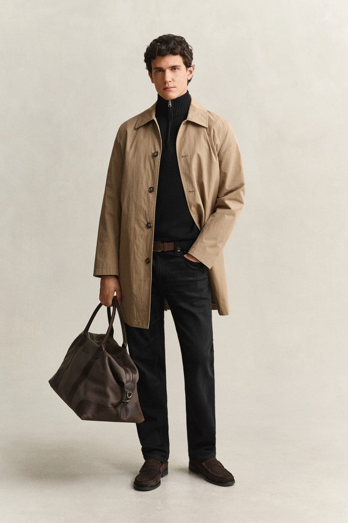 Man wearing a beige trench coat holding a brown bag against a plain background
