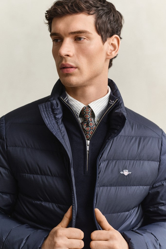 Close up of a man modelling a navy blue GANT puffer jacket with navy quarter zip jumper light shirt and patterned tie