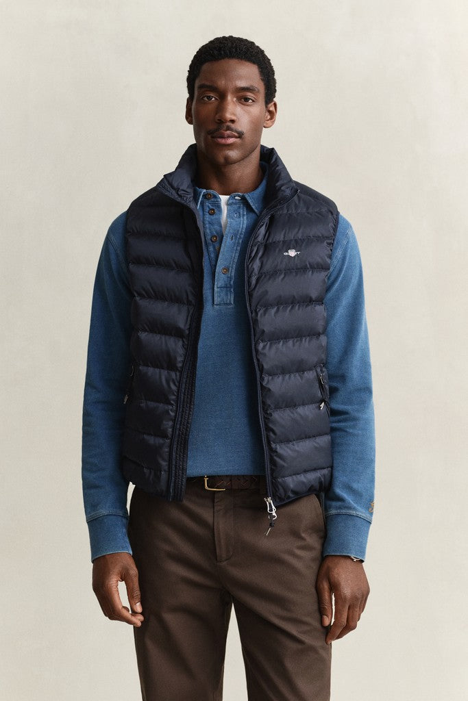 Man modeling a GANT navy blue puffer vest with small GANT logo on the chest over a blue long sleeve polo and brown chinos