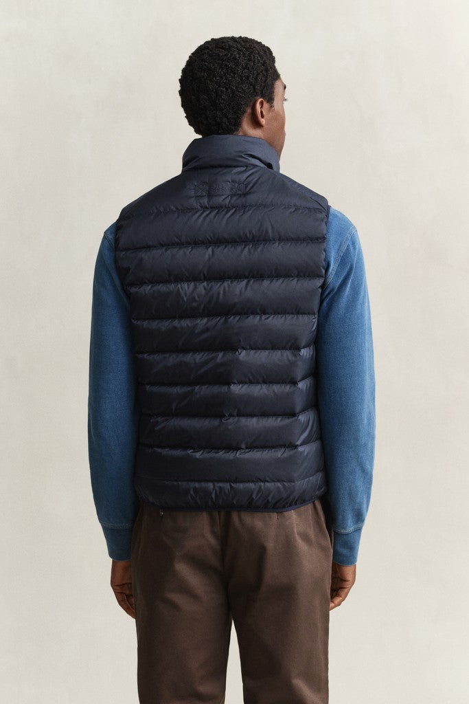 Man wearing a GANT navy blue puffer vest shown from the back with a blue long sleeve top and brown trousers