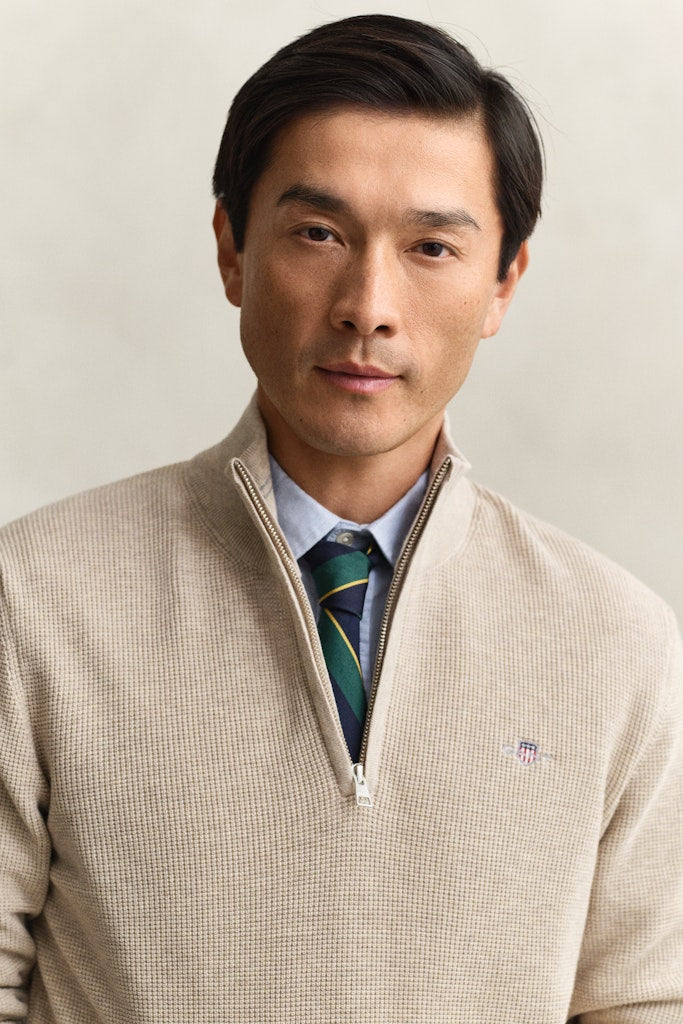 Man wearing a beige sweater with a visible Gant brand logo on a plain background