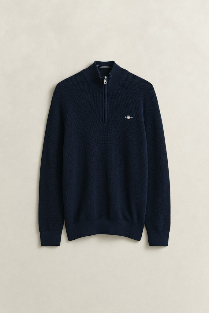 Navy blue sweater with a small Gant logo on a beige background