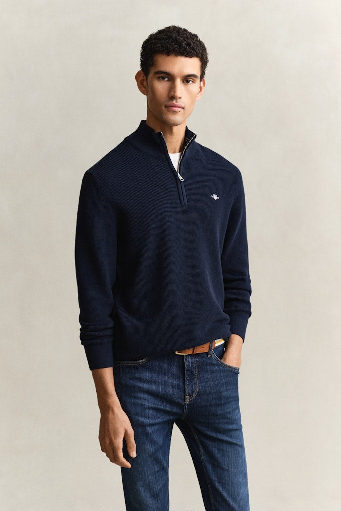 Man wearing a navy blue pullover with a Gant logo on a beige background