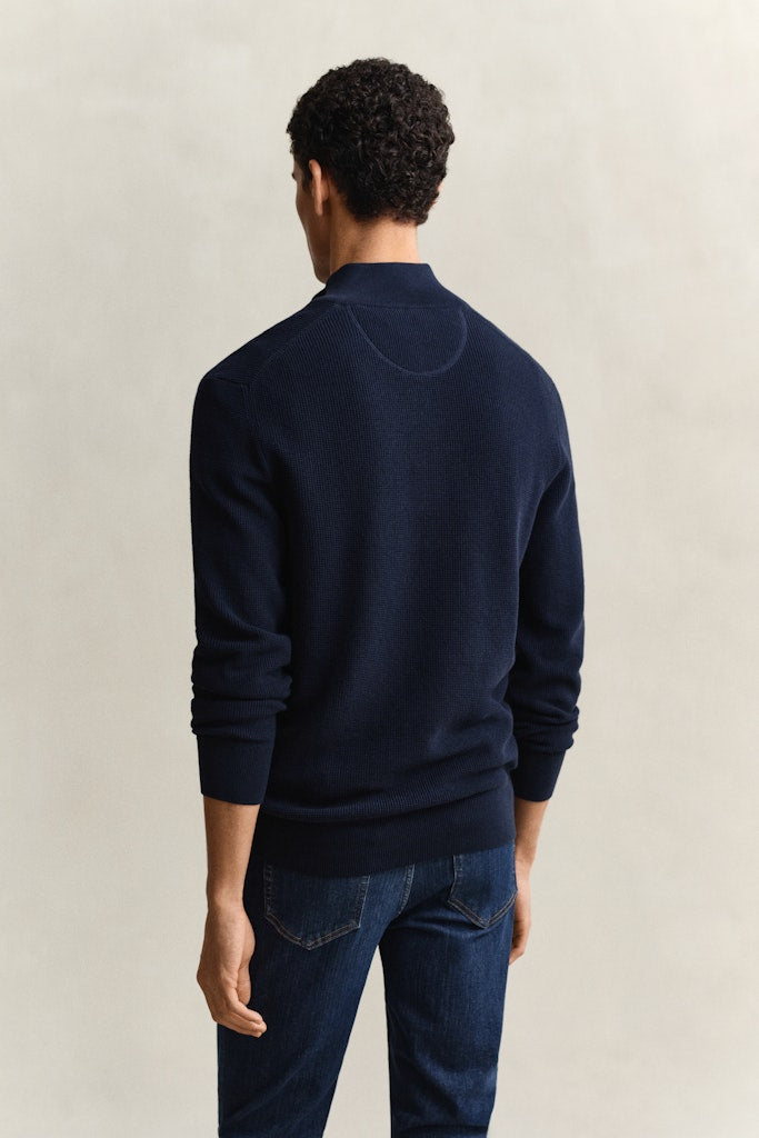 Man wearing a navy blue sweater and jeans against a beige background