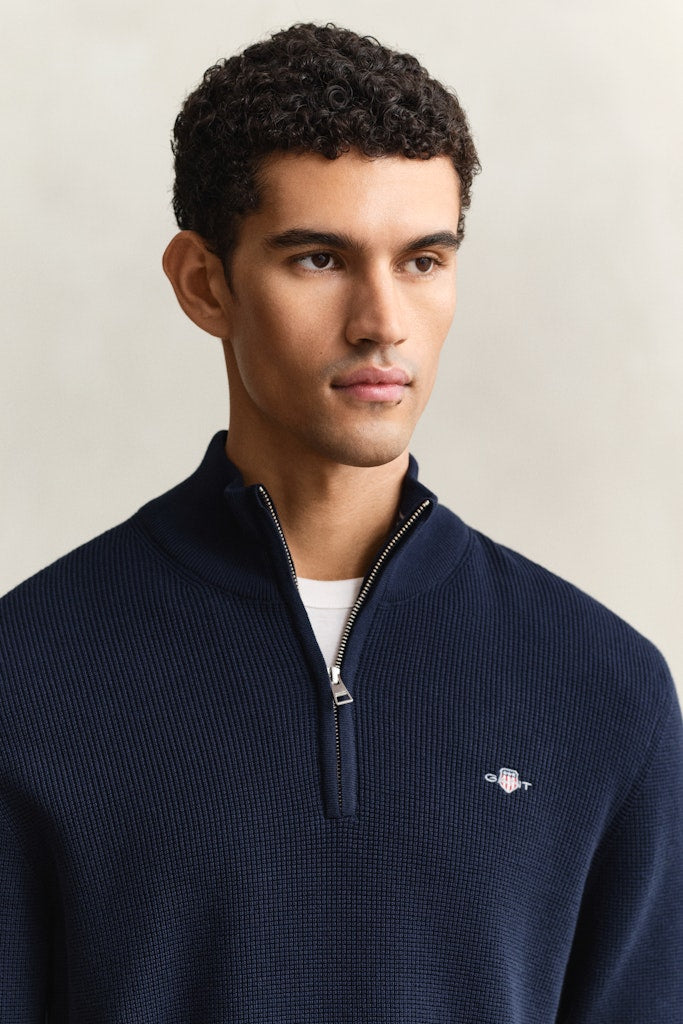 Man wearing a navy blue sweater with a small Gant logo on a beige background