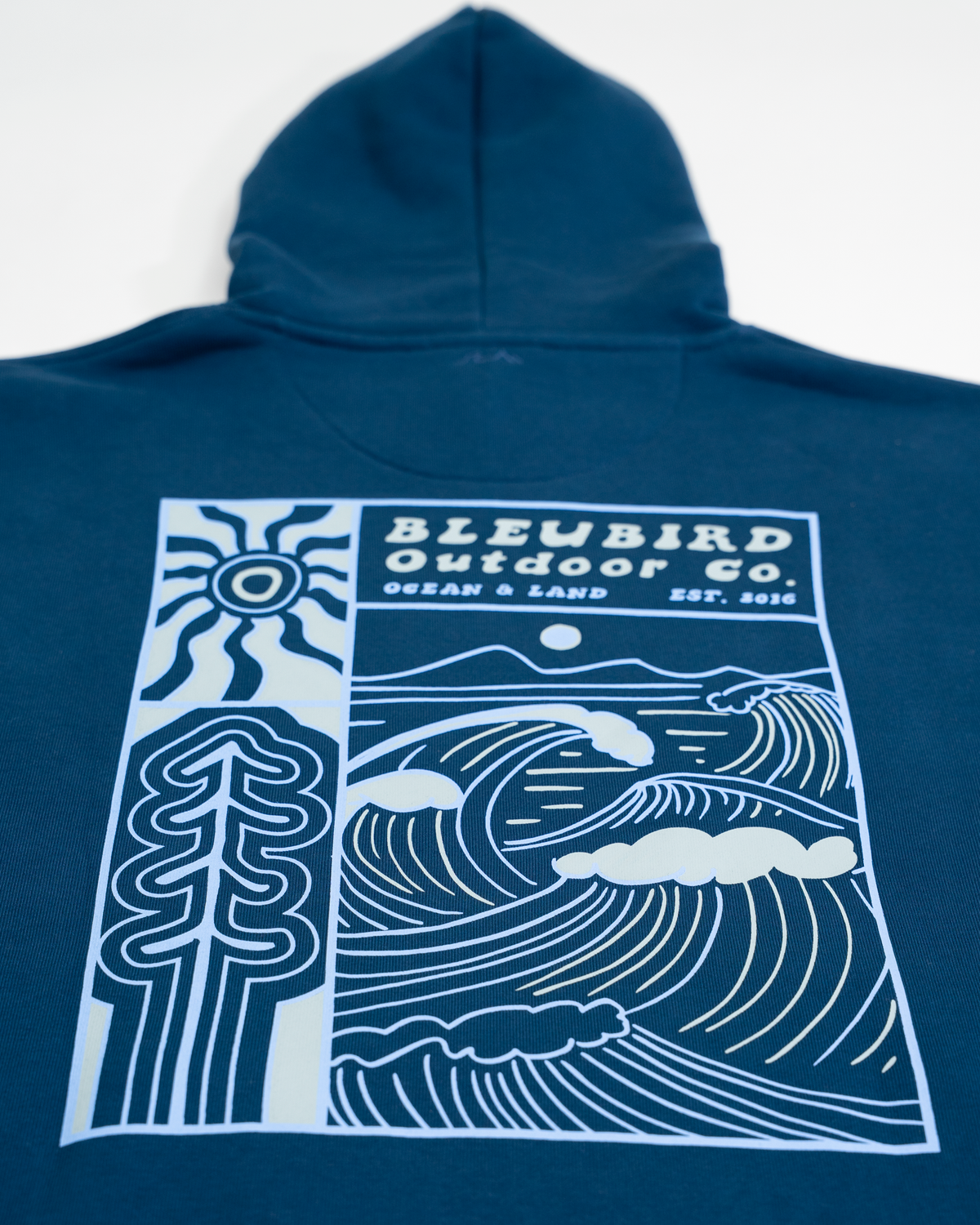 A navy blue hooded sweatshirt laid flat against a white background, featuring a large white graphic print on the back with the text 'BLEUBIRD Outdoor Co' and an illustrated wave, tree, sun, and cloud design.