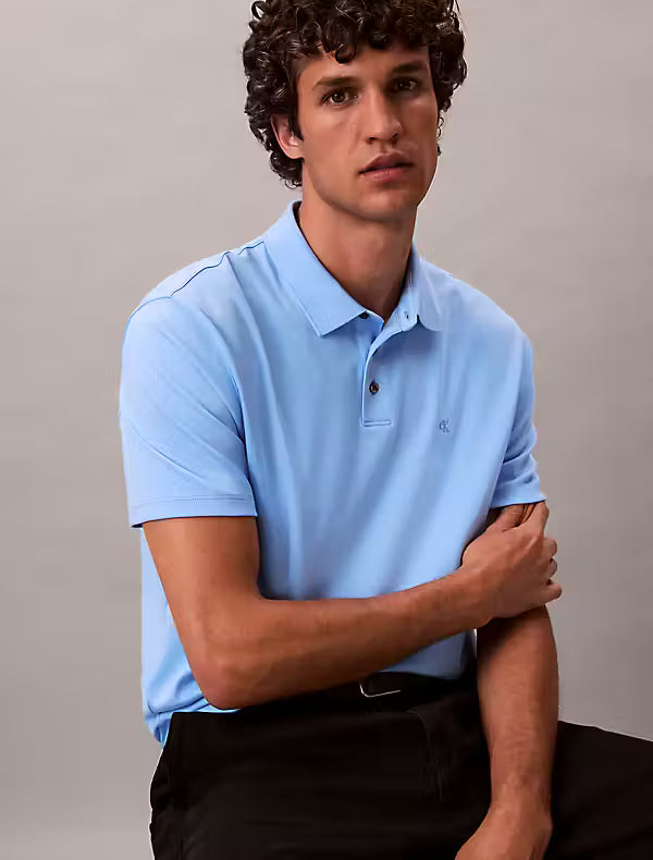 Calvin Klein Supima Cotton Polo. Man wearing a blue CK polo and black trousers on a grey background - Matt O'Brien Fashions