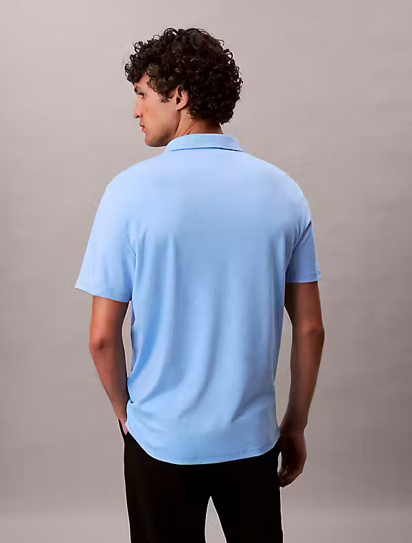 Calvin Klein Supima Cotton Polo. Man wearing a blue polo and black trousers on a grey background - Matt O'Brien Fashions