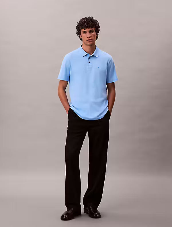 Calvin Klein Supima Cotton Polo. Man wearing a blue polo and black trousers and shoes on a grey background - Matt O'Brien Fashions