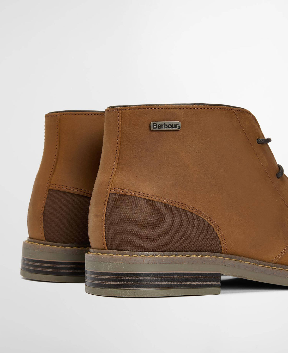 Brown leather boots with a visible Barbour brand logo on a light gray background