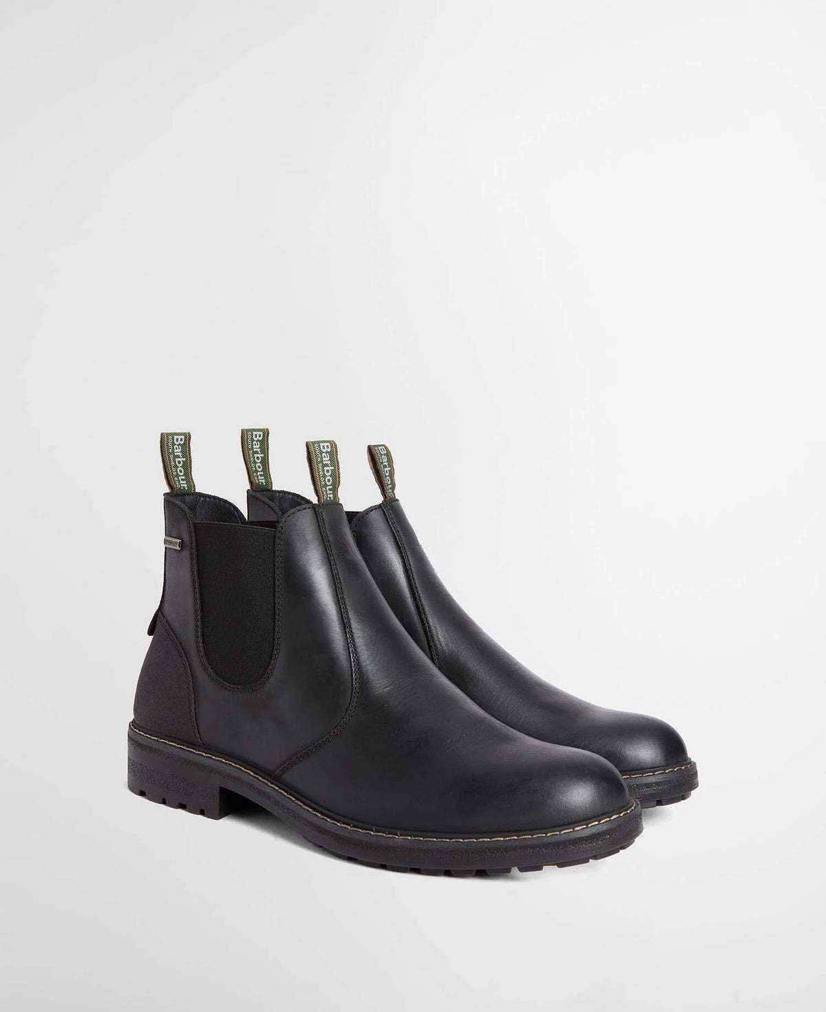 A pair of black leather Chelsea boots with black elastic side panels and olive green pull tabs, photographed on a light gray studio background.