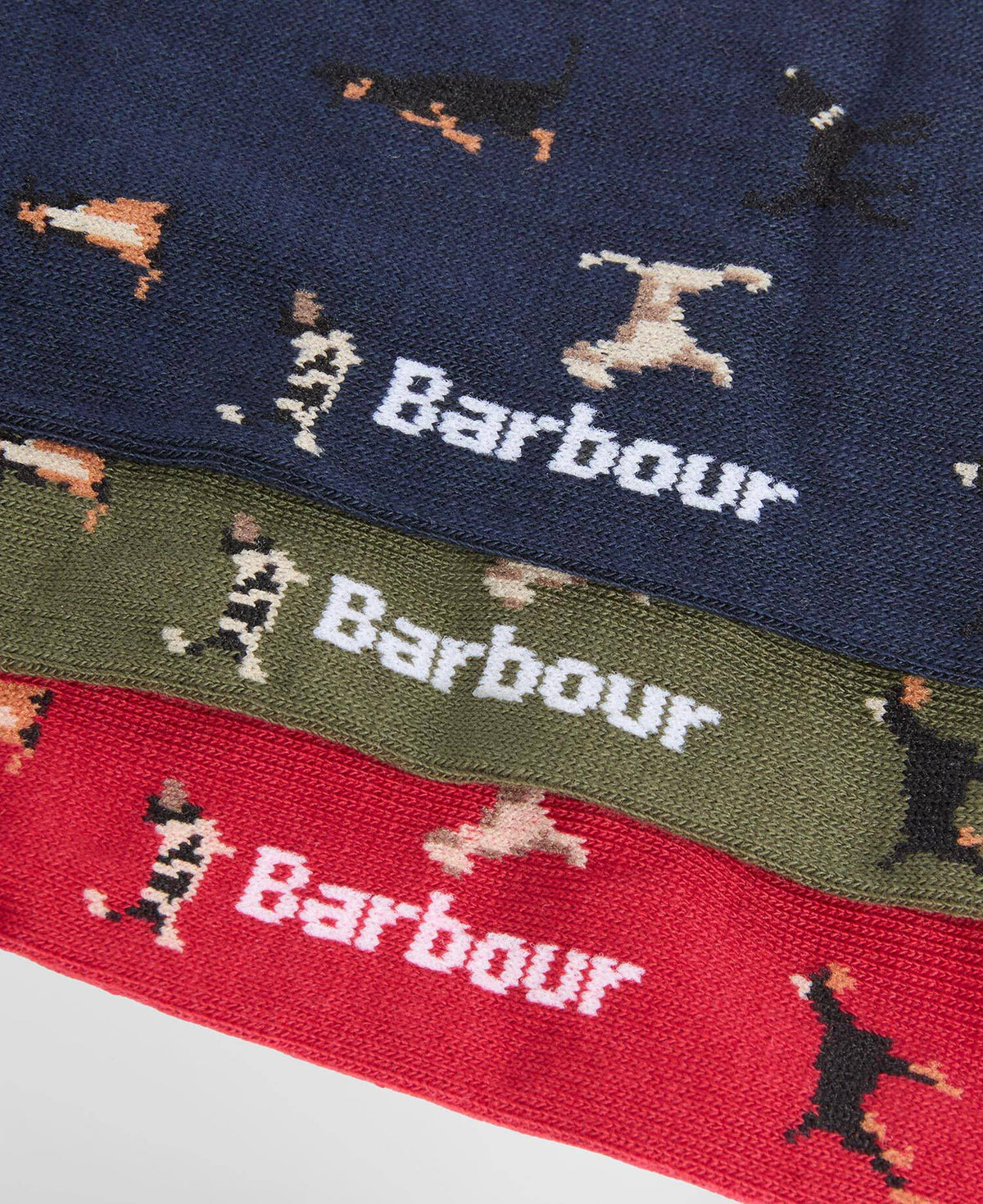Three pairs of knitted socks stacked diagonally, featuring the Barbour logo and dachshund illustrations in navy blue, olive green, and red.