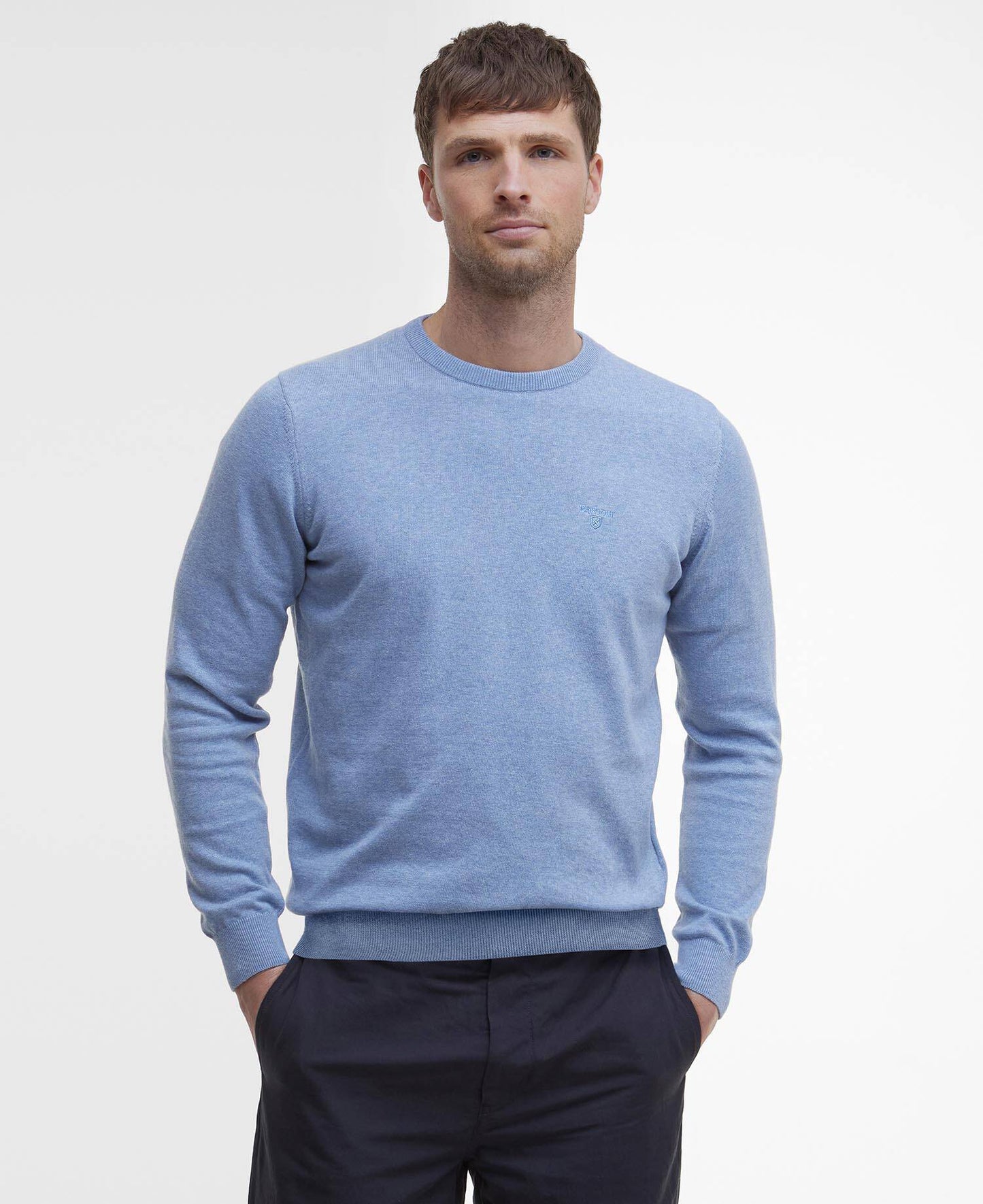 Man wearing a light blue sweater and dark pants on a plain background