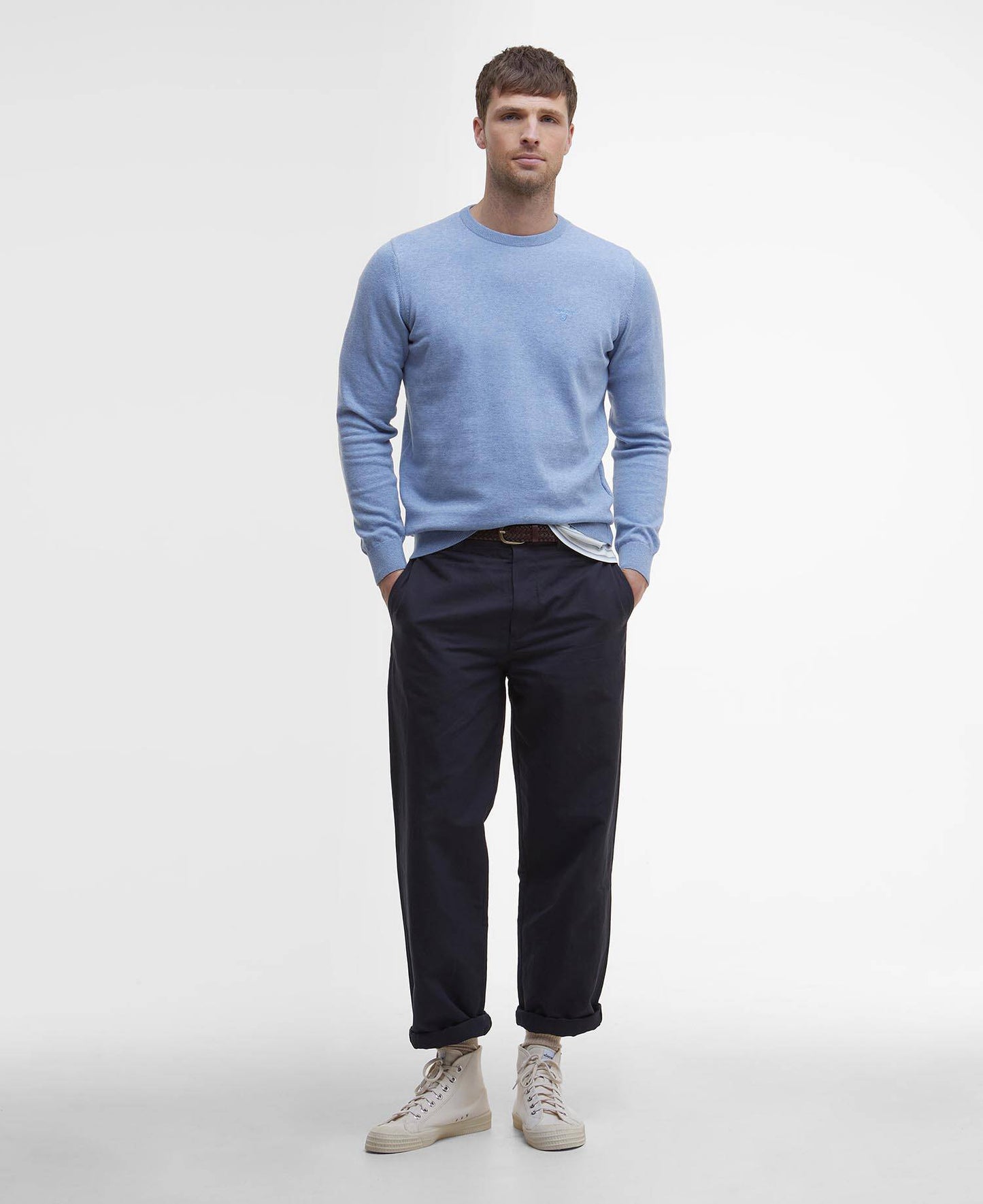 Man wearing a light blue sweater and dark pants on a white background