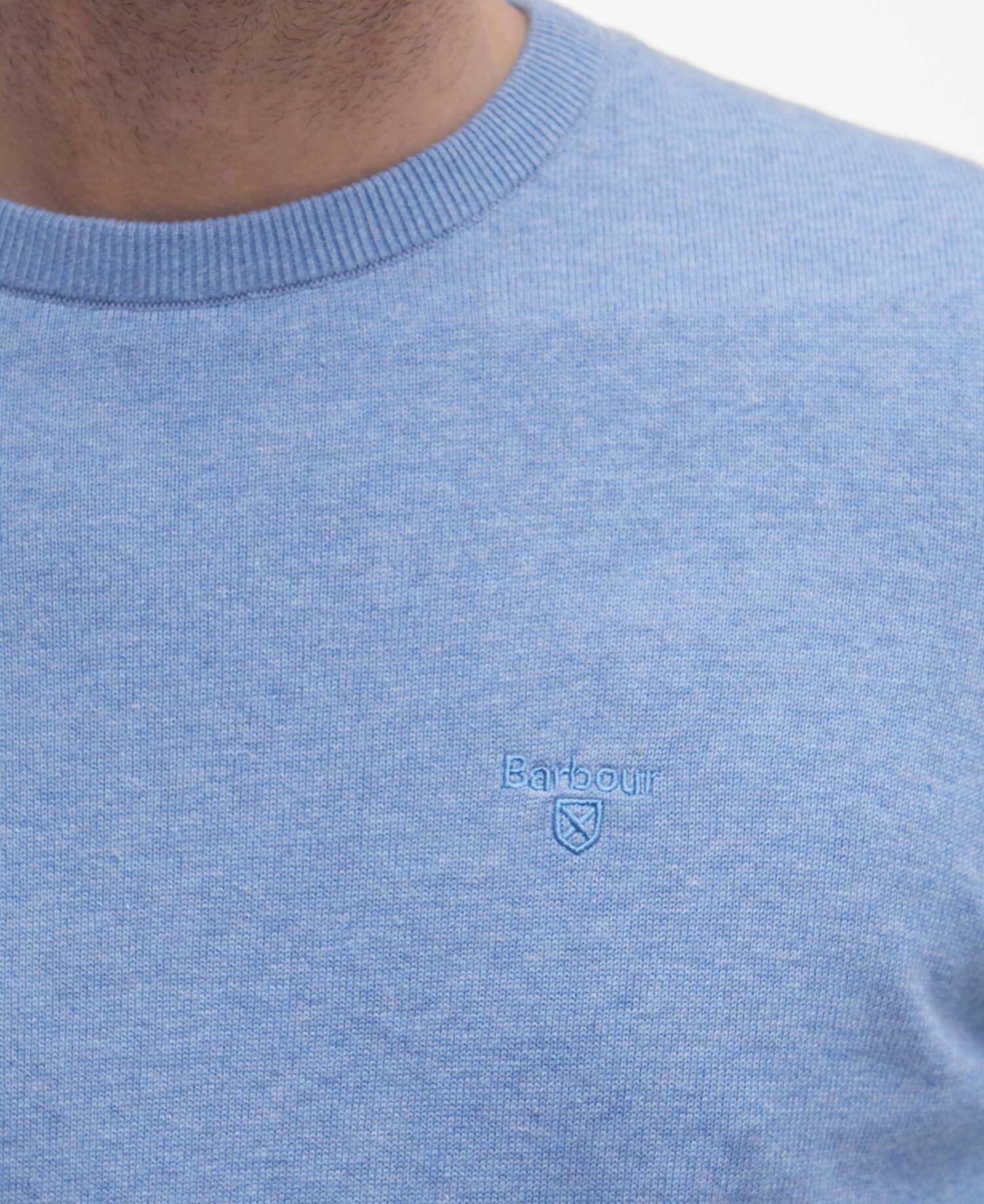 Close-up of a blue sweater with a Barbour brand logo on a white background