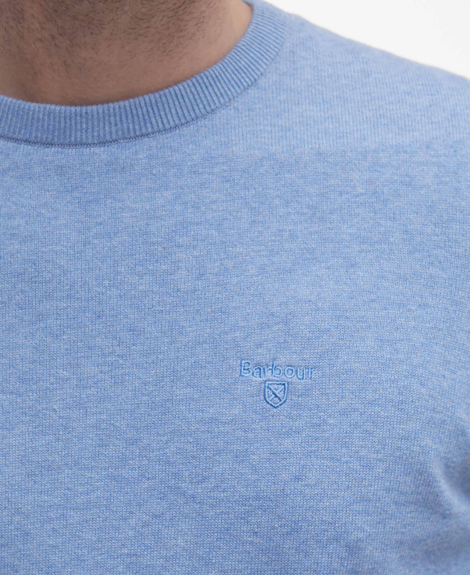 Close-up of a blue sweater with a Barbour brand logo on a white background