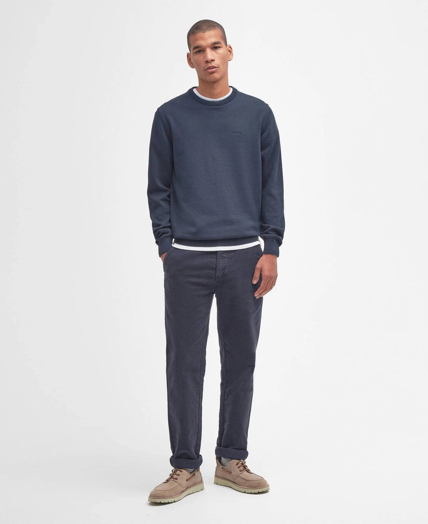 Man wearing a navy sweater and pants with beige shoes on a white background