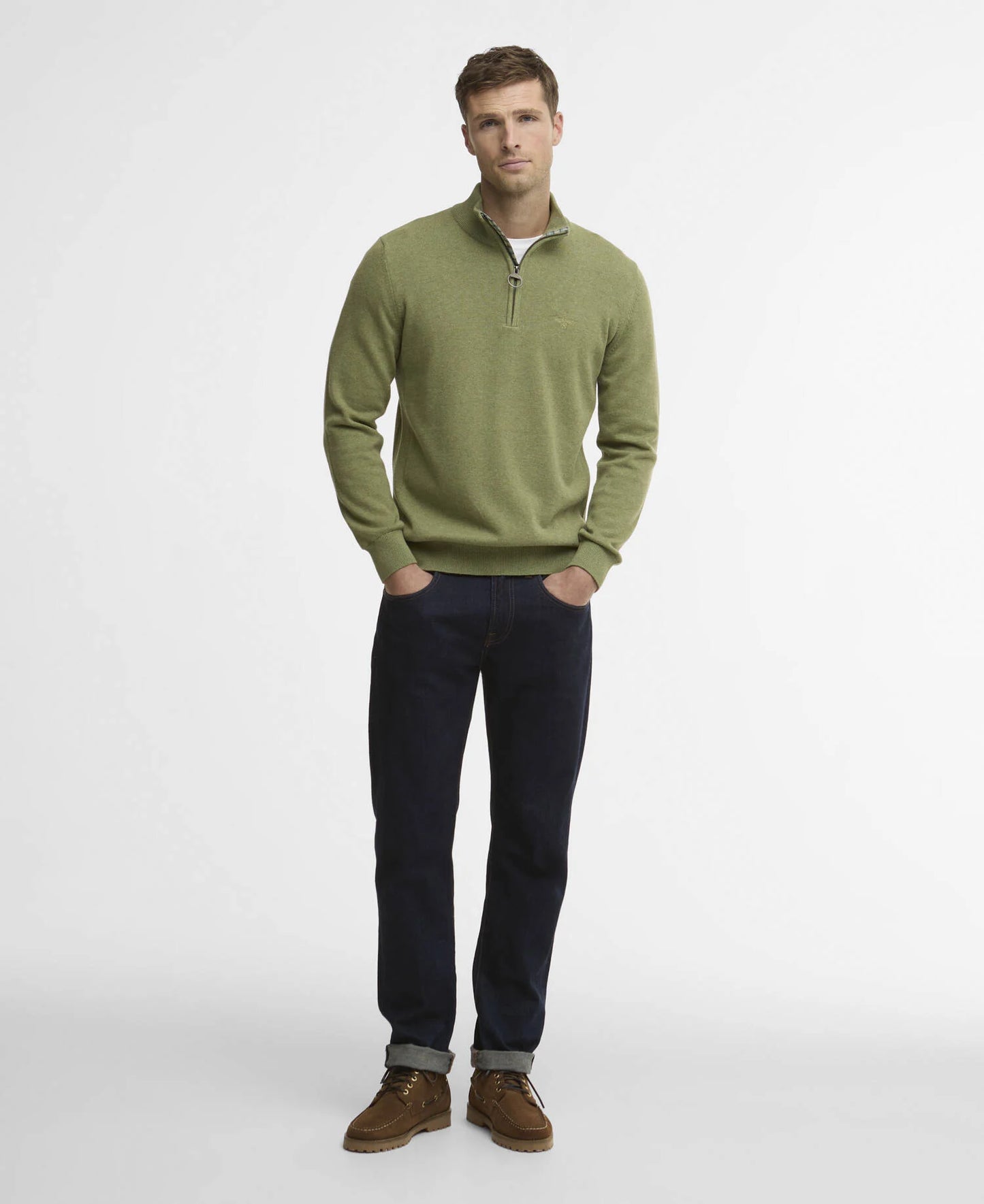Man wearing a green sweater and dark jeans on a white background