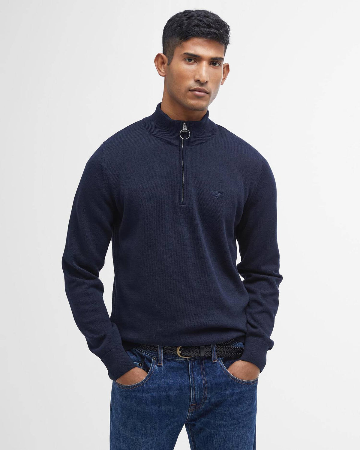 Man wearing a navy half-zip sweater and blue jeans on a light gray background