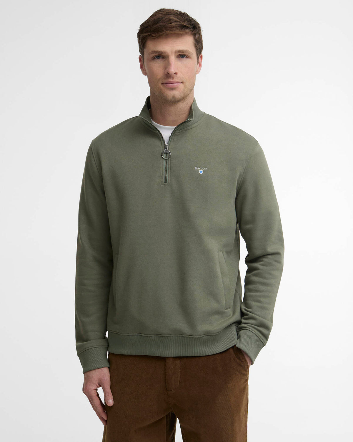 A man wearing an olive green quarter-zip pullover sweatshirt with a small embroidered Barbour logo on the left chest, paired with brown pants, against a plain light gray studio background.