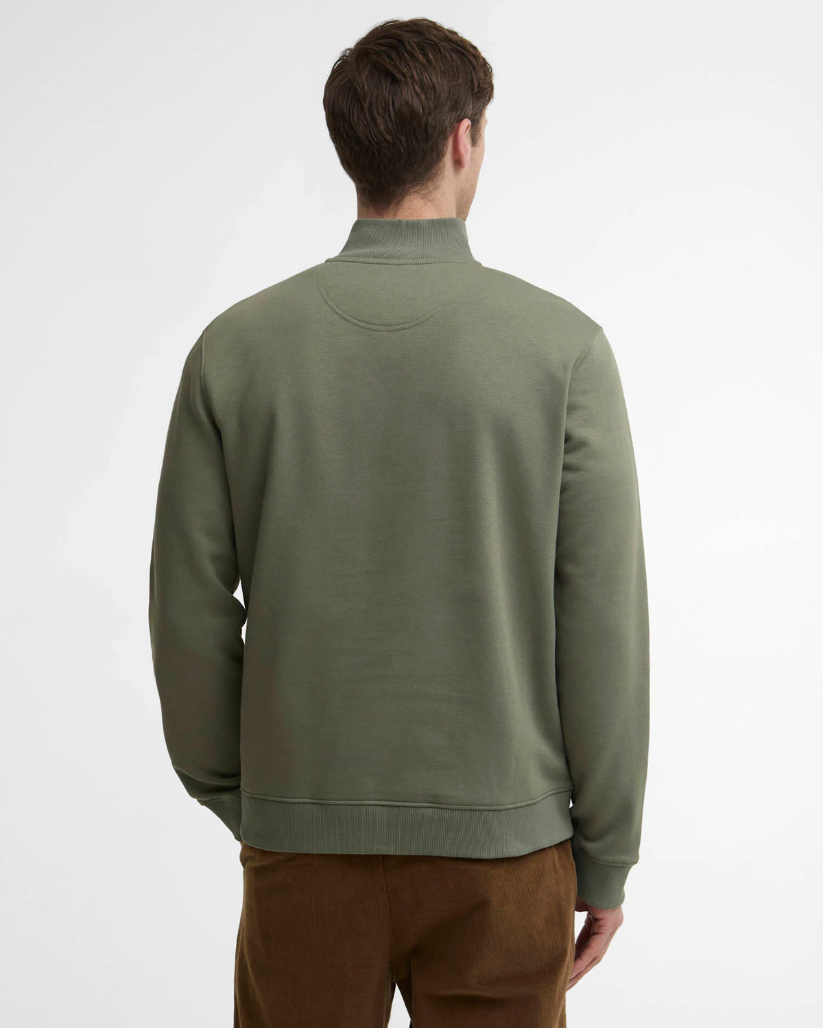 A man viewed from behind wearing an olive green mock neck sweatshirt and brown pants, photographed against a clean white studio background.