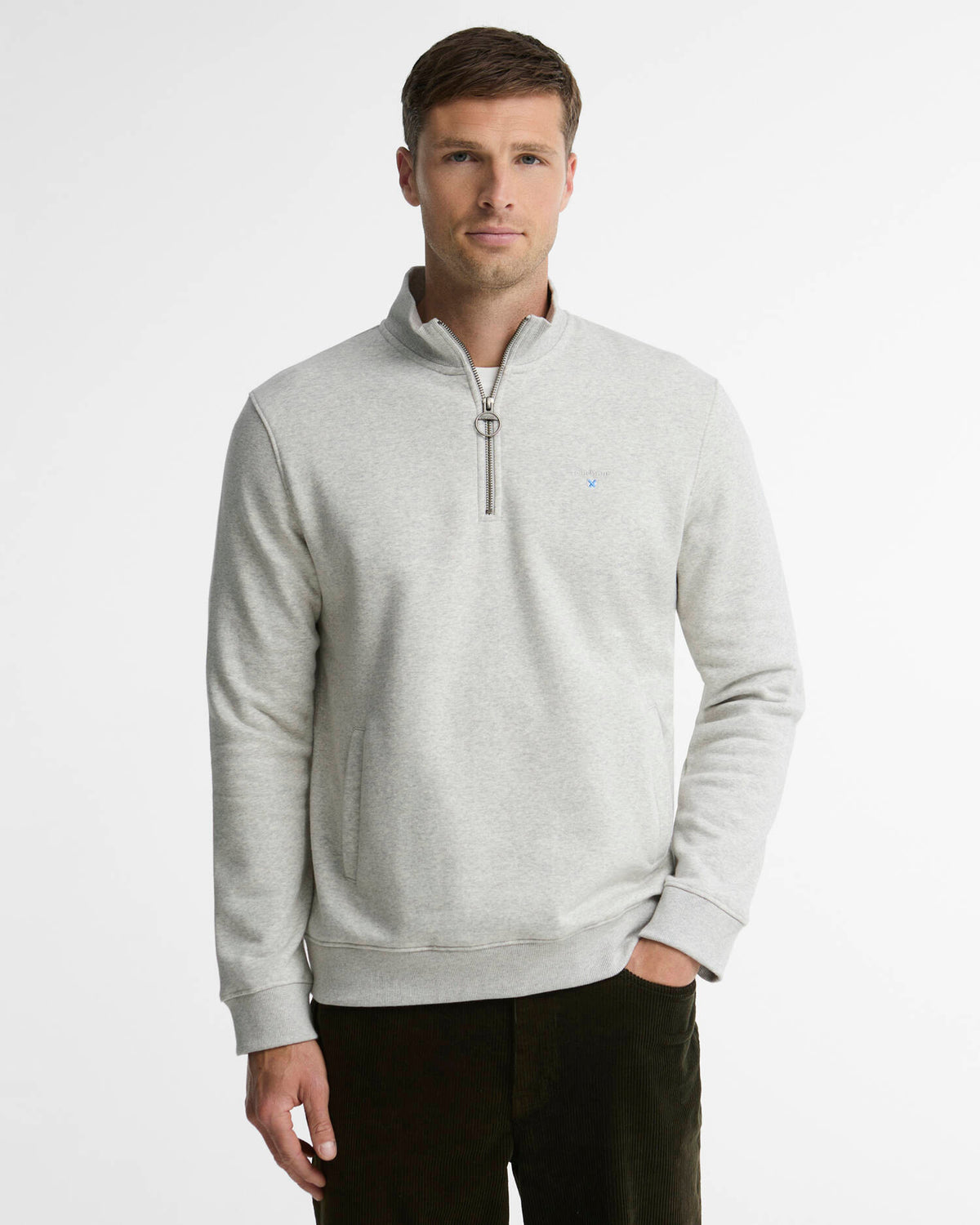 A man wearing a light gray heathered quarter-zip pullover sweatshirt with a small Barbour embroidered logo on the chest, paired with dark pants, against a plain light gray studio background.