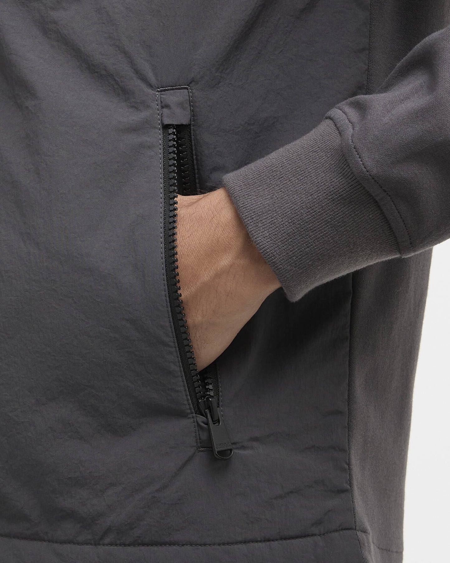Close-up of a dark gray jacket with a zipper, showing a hand reaching in.