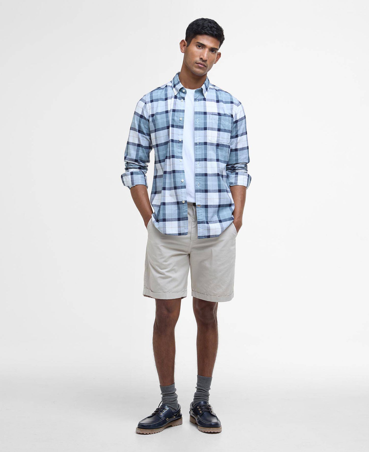 Man wearing a blue plaid shirt, beige shorts, and navy shoes on a white background