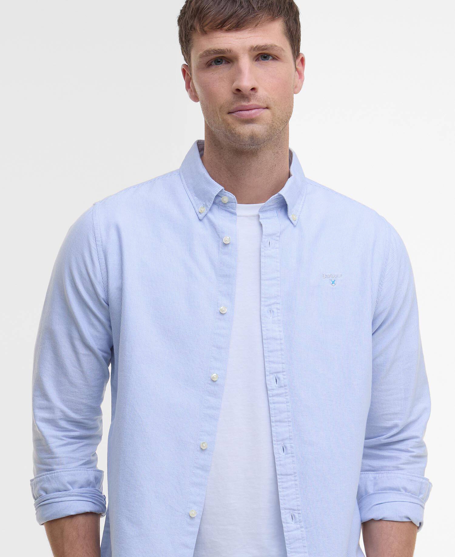 Man wearing a light blue striped shirt with a Barbour logo and a white T-shirt on a white background