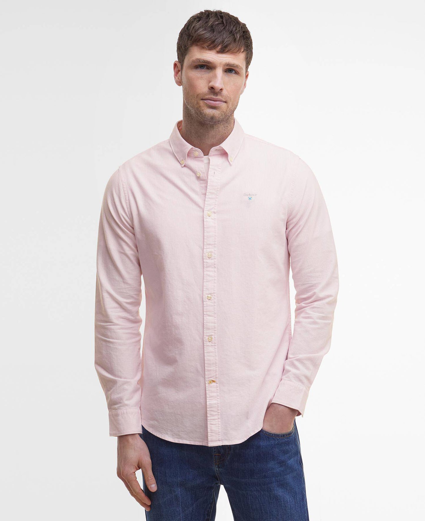 Man wearing a light pink Barbour shirt and blue jeans on a white background