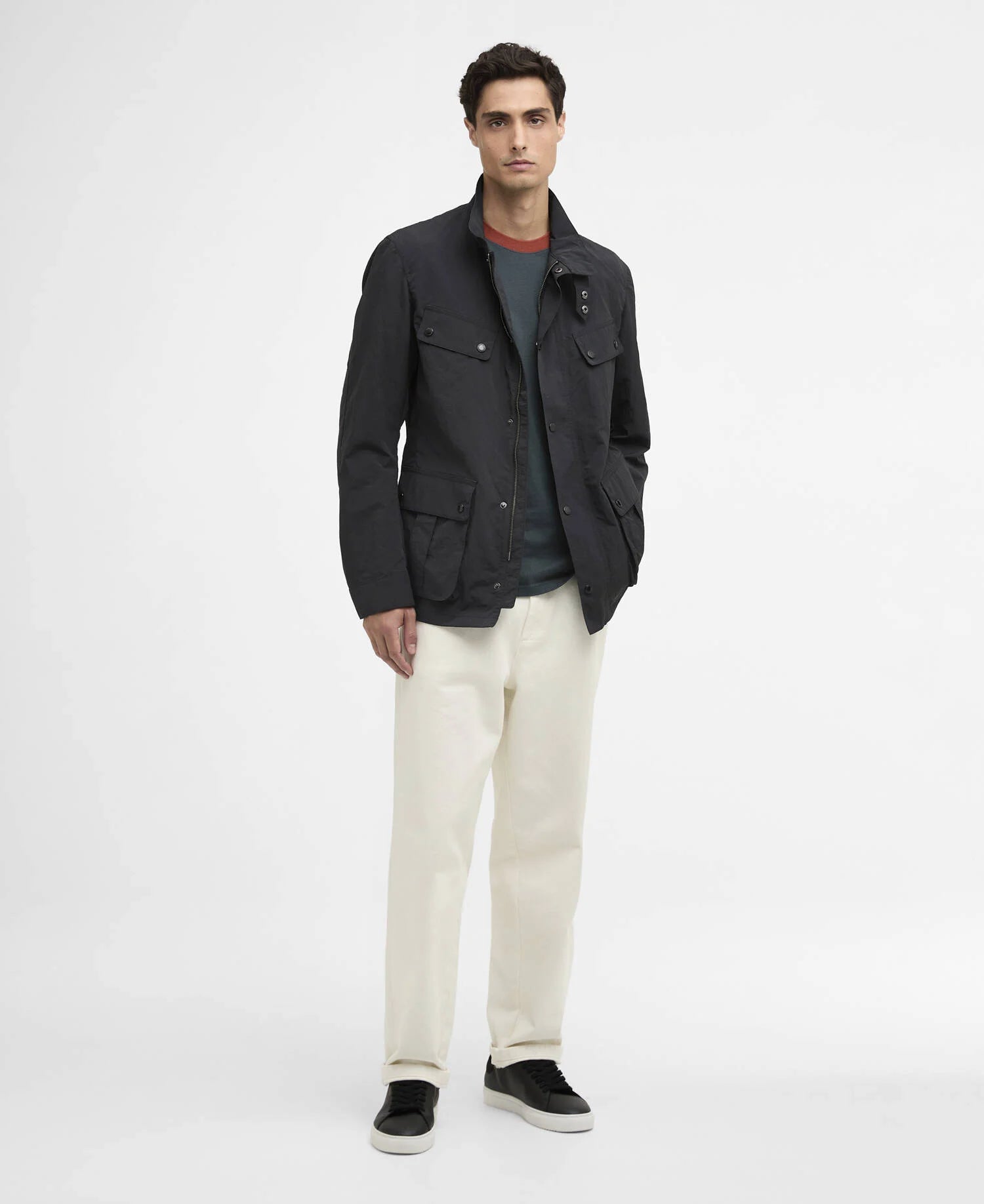 Man wearing a dark jacket, grey T-shirt, white pants, and black shoes on a light gray background